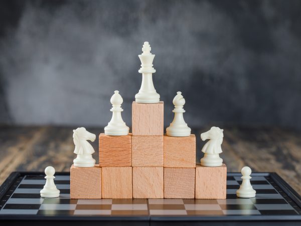 business hierarchy concept with chessboard figures pyramid wooden blocks foggy wooden table side view