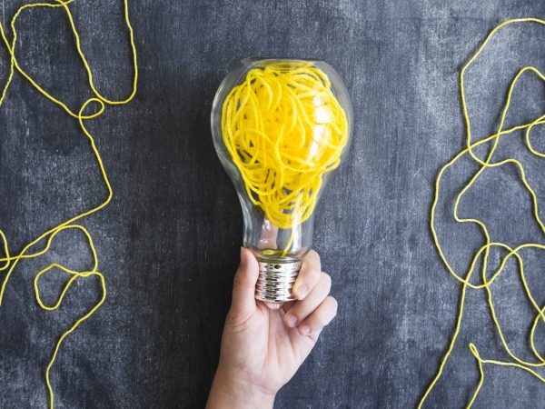 close up hand holding transparent light bulb with yellow yarn blackboard