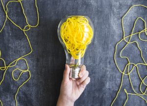close-up-hand-holding-transparent-light-bulb-with-yellow-yarn-blackboard