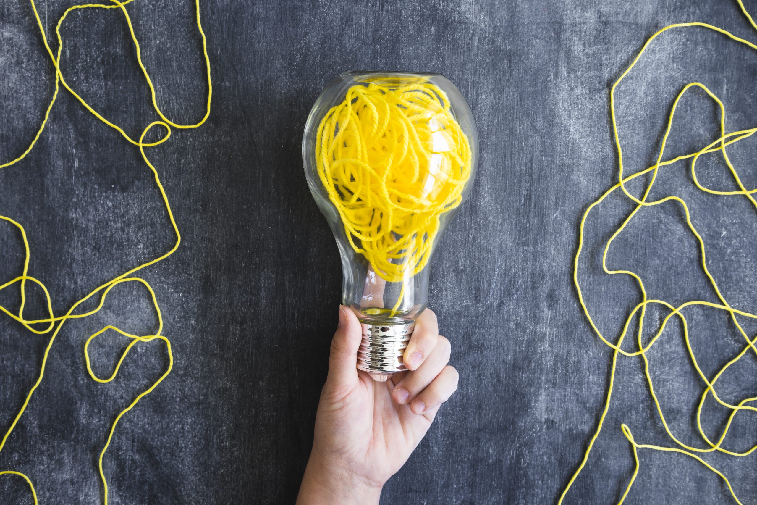 Hizmetler 15 close up hand holding transparent light bulb with yellow yarn blackboard scaled